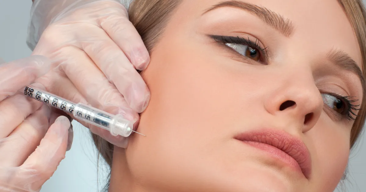 A woman receiving a Kybella injection in the lower cheek and jawline area to reduce jowls